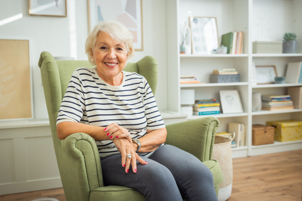 Mature woman at home. She is sitting in armchair and looking at camera.